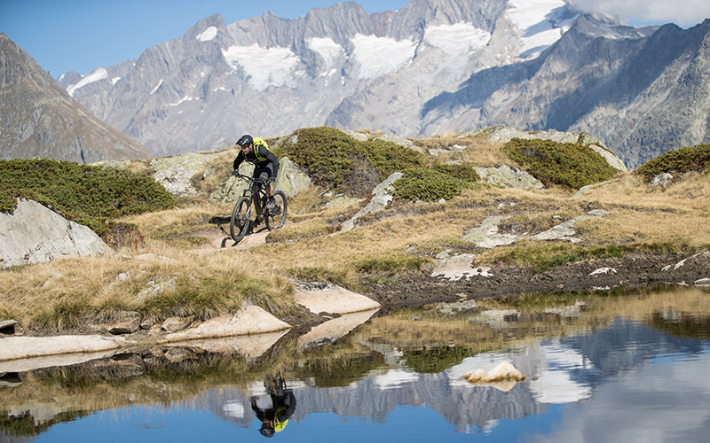Bergstrom: Freiheit auf zwei Rädern inmitten der Alpen. Mountainbiker auf einem Bergstrom E-Bike überquert einen kleinen Bach vor einer beeindruckenden Bergkulisse.
