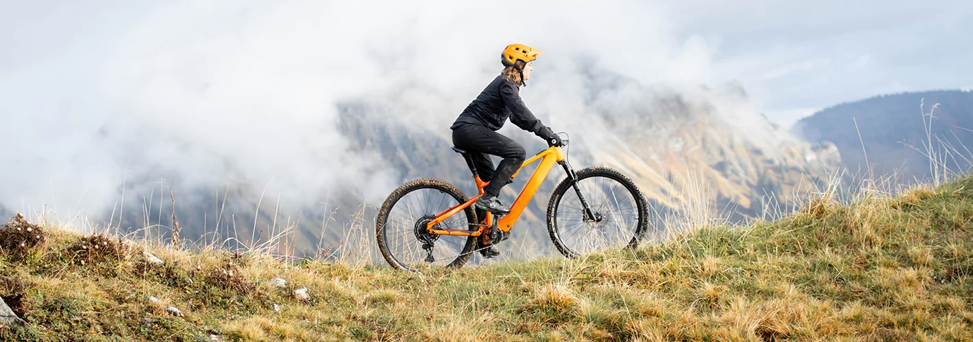 Bergstrom Flow: Erlebe den Flow Frau auf orangenem Bergstrom Flow E-Mountainbike vor der Kulisse der Schweizer Alpen.