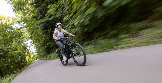 Conduite rapide avec le vélo électrique SUV ATV C de Bergstrom : dynamisme et style réunis Une femme roule de manière dynamique sur un vélo électrique SUV ATV C de Bergstrom sur un chemin dans un environnement verdoyant.