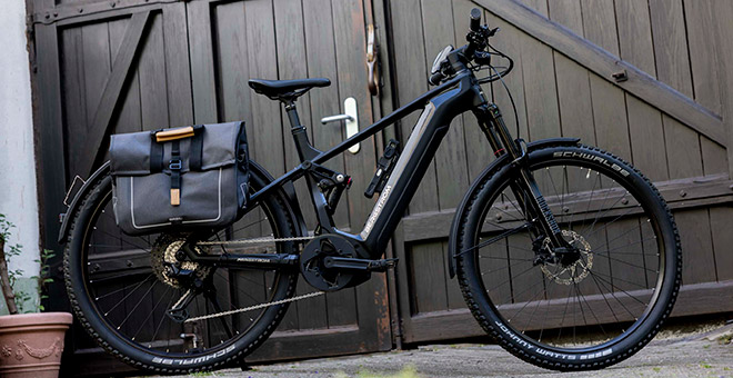 Le vélo électrique SUV ATV C de Bergstrom : une beauté classique. Le vélo électrique SUV ATV C noir de Bergstrom avec ses sacoches devant une porte de garage en bois sombre.