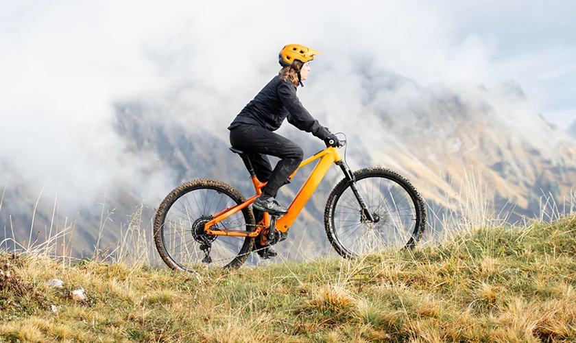Bergstrom Flow: Erlebe den Flow Frau auf orangenem Bergstrom Flow E-Mountainbike vor der Kulisse der Schweizer Alpen.